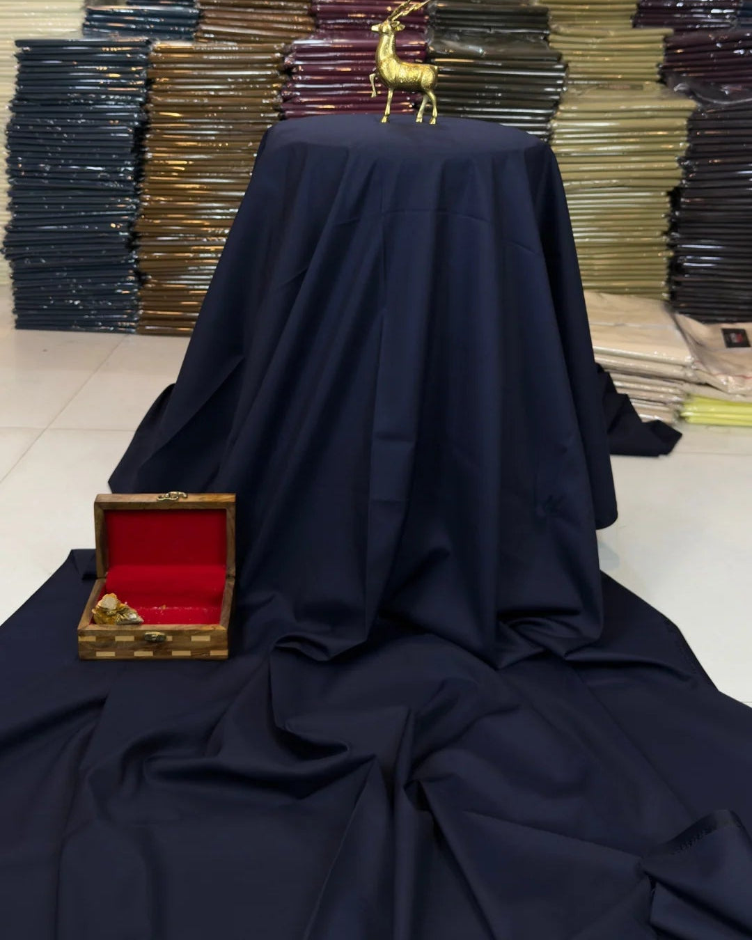 Stacks of folded fabric with a table draped in navy cloth and a small box in the foreground.